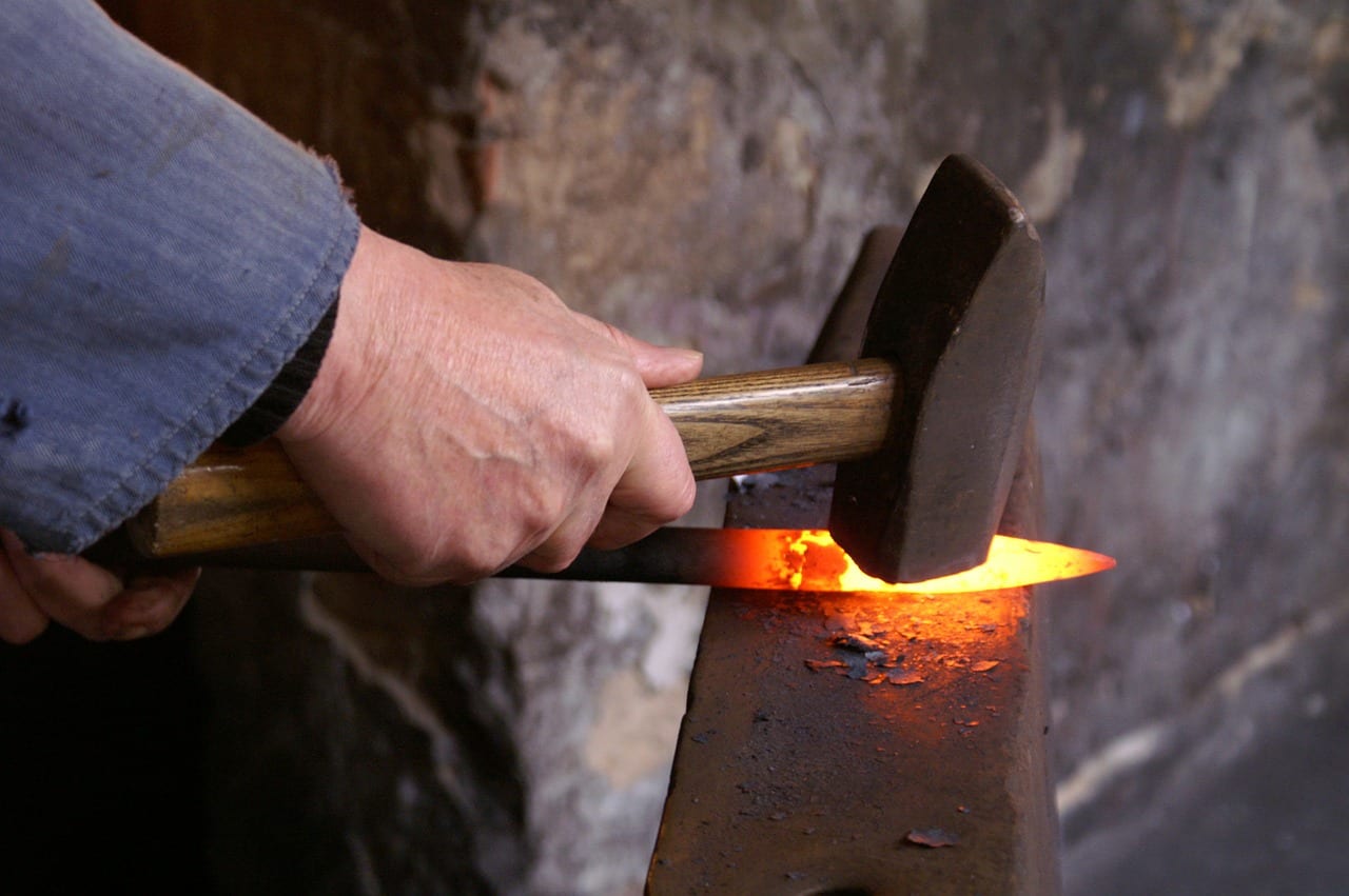 Hammering hot metal on an anvil in a forge